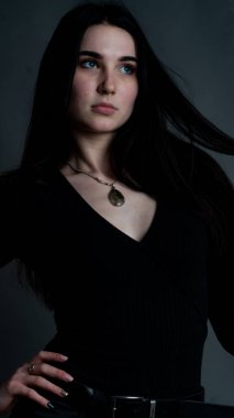 Karanlık stüdyoda şık giyinmiş esmer bir kadın poz veriyor.  