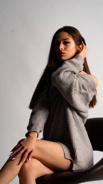 Güzel seksi kız, kısa gri bir elbise, beyaz bir arka plan sandalyesi