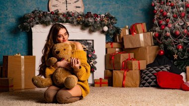 Noel süslemeli stüdyoda şöminenin yanında poz veren güzel esmer genç bir kadın. 