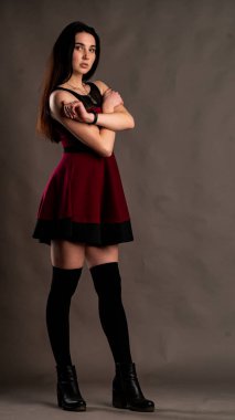 Karanlık stüdyoda şık giyinmiş esmer bir kadın poz veriyor.  