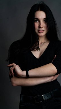 Karanlık stüdyoda şık giyinmiş esmer bir kadın poz veriyor.  