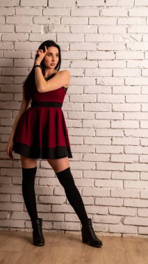 Koyu renk saçlı, kırmızı elbiseli, karanlık stüdyoda poz veren genç ve seksi bir kadın..