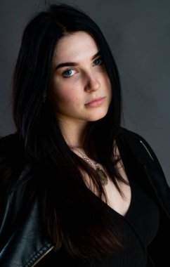 Karanlık stüdyoda şık giyinmiş esmer bir kadın poz veriyor.  