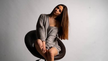 Güzel seksi kız, kısa gri bir elbise, beyaz bir arka plan sandalyesi