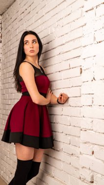 Koyu renk saçlı, kırmızı elbiseli, karanlık stüdyoda poz veren genç ve seksi bir kadın..