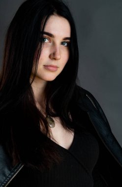 Karanlık stüdyoda şık giyinmiş esmer bir kadın poz veriyor.  