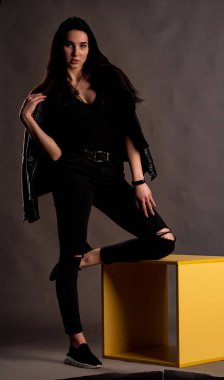 Karanlık stüdyoda şık giyinmiş esmer bir kadın poz veriyor.  