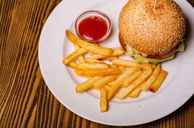 Lezzetli hamburger ve patates kızartması tabakta, ahşap masa arkasında. Sağlıksız gıda konsepti