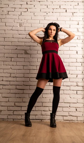 Koyu renk saçlı, kırmızı elbiseli, karanlık stüdyoda poz veren genç ve seksi bir kadın..