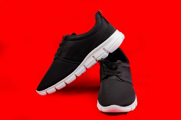 Peligro de nuevos zapatos de deporte negro sin marca o zapatillas aisladas en el fondo rojo con carril de peaje. — Foto de Stock