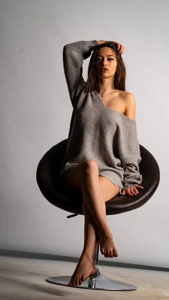 Hermosa chica sexy, con un vestido gris corto, una silla de fondo blanca. —  Fotos de Stock