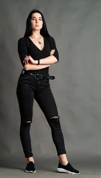 Portrait d'une jeune brune assise sur une chaise haute en bois aux jambes croisées. Fille à la mode portant un pantalon large pour les jambes. Photo prise en studio sur fond gris — Photo