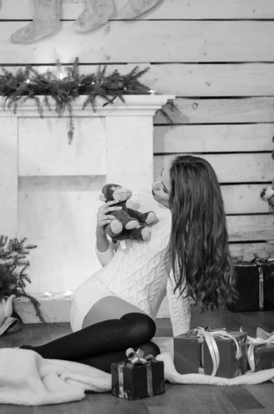 Beautiful sexy woman with Xmas tree in background sitting on elegant chair in cozy scenery. Portrait of girl posing pretty  short tight fit white dress. Attractive brunette female, indoor shot. — Stok fotoğraf