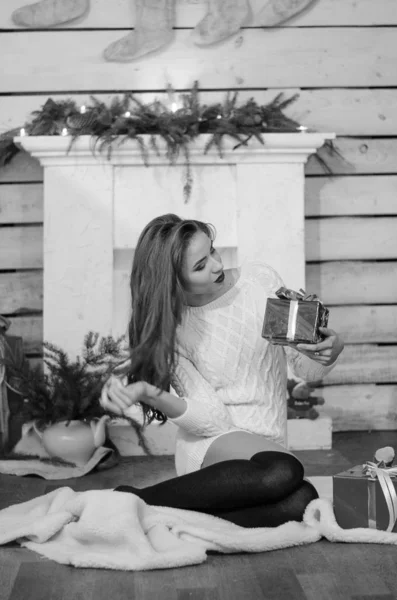 Beautiful sexy woman with Xmas tree in background sitting on elegant chair in cozy scenery. Portrait of girl posing pretty  short tight fit white dress. Attractive brunette female, indoor shot. — Stok fotoğraf