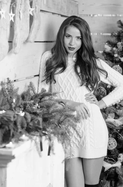 Beautiful sexy woman with Xmas tree in background sitting on elegant chair in cozy scenery. Portrait of girl posing pretty  short tight fit white dress. Attractive brunette female, indoor shot. — Stok fotoğraf