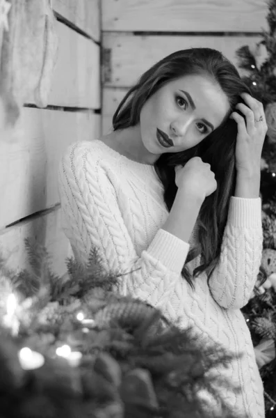 Belle femme sexy avec arbre de Noël en arrière-plan assis sur une chaise élégante dans un décor confortable. Portrait de fille posant robe blanche assez courte ajustement serré. Attrayant brunette femelle, plan intérieur . — Photo
