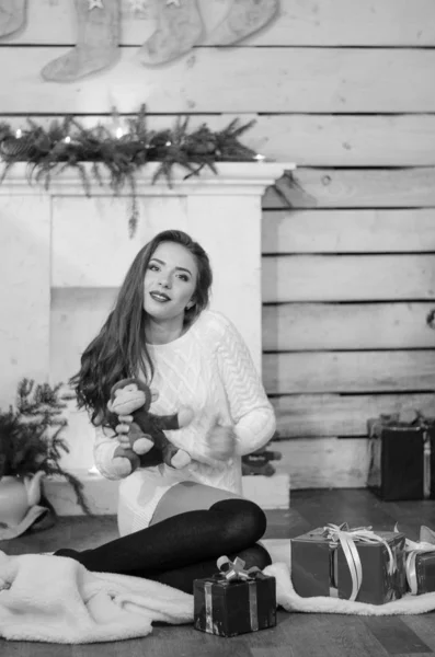 Beautiful sexy woman with Xmas tree in background sitting on elegant chair in cozy scenery. Portrait of girl posing pretty  short tight fit white dress. Attractive brunette female, indoor shot. — Stok fotoğraf