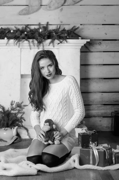 Schöne sexy Frau mit Weihnachtsbaum im Hintergrund sitzt auf eleganten Stuhl in gemütlicher Landschaft. Porträt von Mädchen posiert ziemlich kurz eng anliegendes weißes Kleid. attraktive brünette weiblich, indoor shot. — Stockfoto