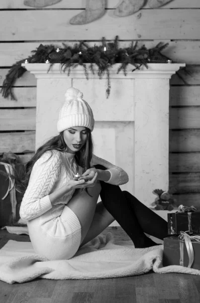 Beautiful sexy woman with Xmas tree in background sitting on elegant chair in cozy scenery. Portrait of girl posing pretty  short tight fit white dress. Attractive brunette female, indoor shot. — Stok fotoğraf