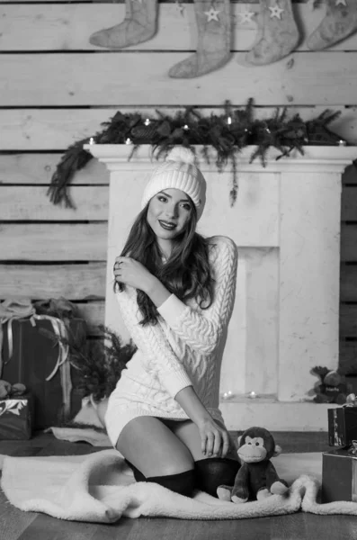 Beautiful sexy woman with Xmas tree in background sitting on elegant chair in cozy scenery. Portrait of girl posing pretty  short tight fit white dress. Attractive brunette female, indoor shot. — Stok fotoğraf