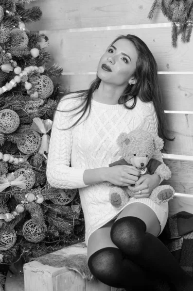 Сексуальная женщина с рождественской елкой на заднем плане, сидящая на элегантном стуле в уютной сцене. Портрет девушки, позирующей довольно коротко облегающим белым платьем. Привлекательная брюнетка женского пола, снимок в помещении . — стоковое фото