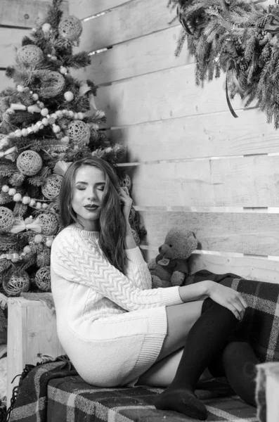 Hermosa mujer sexy con árbol de Navidad en el fondo sentado en una silla elegante en un paisaje acogedor. Retrato de niña posando vestido blanco ajustado bastante corto. Atractiva morena femenina, tiro de interior . —  Fotos de Stock