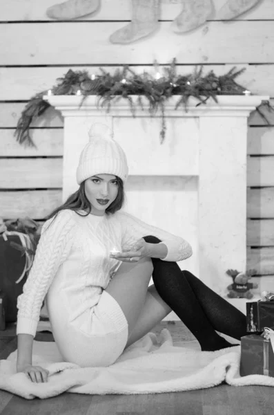 Beautiful sexy woman with Xmas tree in background sitting on elegant chair in cozy scenery. Portrait of girl posing pretty  short tight fit white dress. Attractive brunette female, indoor shot. — Stok fotoğraf