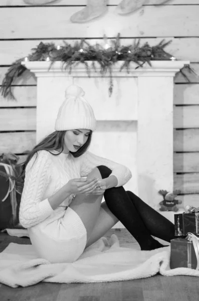 Beautiful sexy woman with Xmas tree in background sitting on elegant chair in cozy scenery. Portrait of girl posing pretty  short tight fit white dress. Attractive brunette female, indoor shot. — Stok fotoğraf