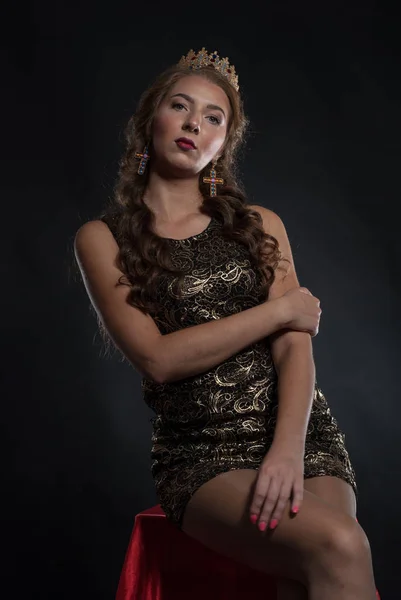 Beautiful young woman with crown on head posing in studio