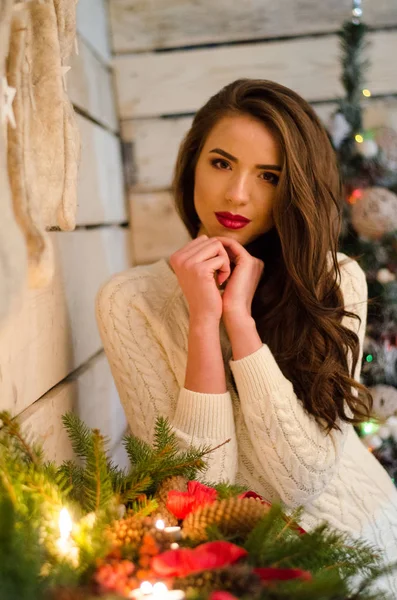 Gyönyörű szexi nő karácsonyfa a háttérben ül elegáns szék hangulatos táj. Portré lány pózol elég rövid feszes fehér ruhát. Vonzó barna nő, beltéri lövés. — Stock Fotó