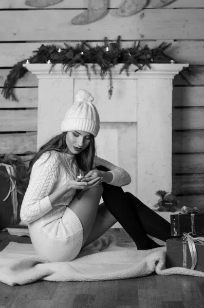 Beautiful sexy woman with Xmas tree in background sitting on elegant chair in cozy scenery. Portrait of girl posing pretty  short tight fit white dress. Attractive brunette female, indoor shot. — Stok fotoğraf