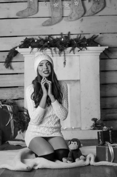 Mulher sexy bonita com árvore de Natal no fundo sentado em cadeira elegante em cenário acolhedor. Retrato de menina posando muito curto vestido branco ajuste apertado. Mulher morena atraente, tiro em casa . — Fotografia de Stock