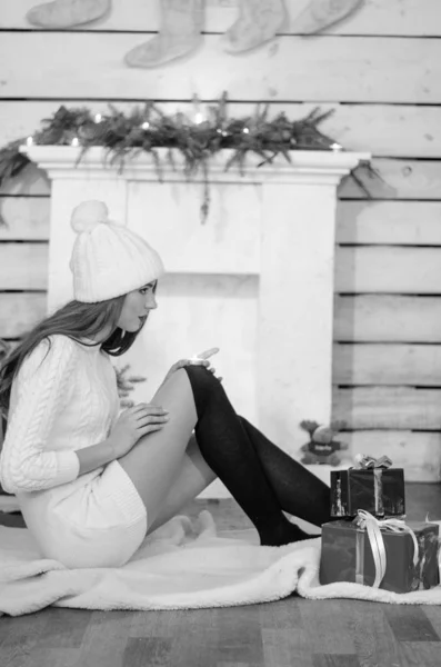 Beautiful sexy woman with Xmas tree in background sitting on elegant chair in cozy scenery. Portrait of girl posing pretty  short tight fit white dress. Attractive brunette female, indoor shot. — 스톡 사진