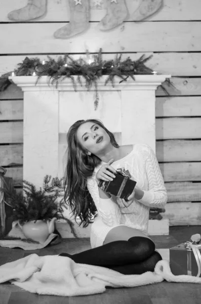 Beautiful sexy woman with Xmas tree in background sitting on elegant chair in cozy scenery. Portrait of girl posing pretty  short tight fit white dress. Attractive brunette female, indoor shot. — Stok fotoğraf