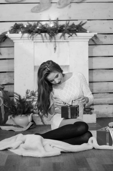 Beautiful sexy woman with Xmas tree in background sitting on elegant chair in cozy scenery. Portrait of girl posing pretty  short tight fit white dress. Attractive brunette female, indoor shot. — Stok fotoğraf