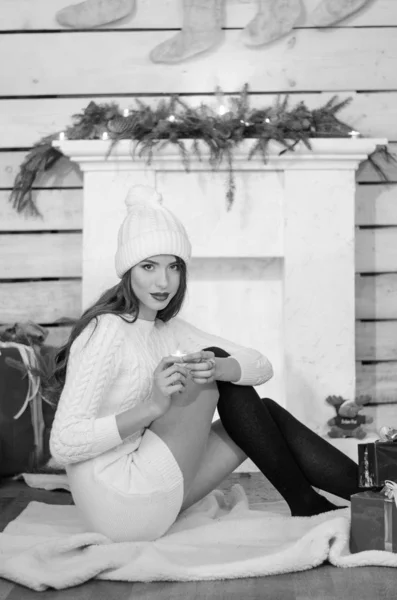 Beautiful sexy woman with Xmas tree in background sitting on elegant chair in cozy scenery. Portrait of girl posing pretty  short tight fit white dress. Attractive brunette female, indoor shot. — Stok fotoğraf