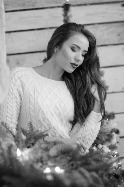 Beautiful sexy woman with Xmas tree in background sitting on elegant chair in cozy scenery. Portrait of girl posing pretty  short tight fit white dress. Attractive brunette female, indoor shot. — Stok fotoğraf