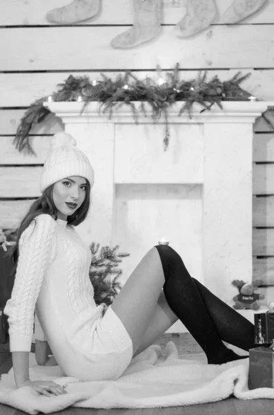 Beautiful sexy woman with Xmas tree in background sitting on elegant chair in cozy scenery. Portrait of girl posing pretty  short tight fit white dress. Attractive brunette female, indoor shot. — Stok fotoğraf