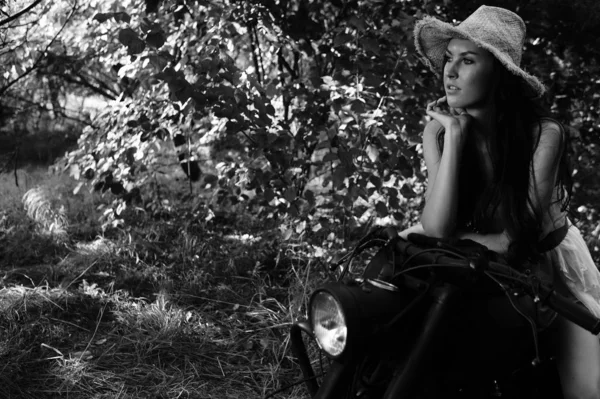 Young sexy woman with long wavy hair in leather clothes and sunglasses posing near a motorcycle. Black and white photo. — Stock Photo, Image