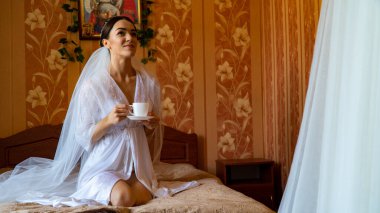 Beyaz elbiseli gelin düğünden önce odada poz veriyor.