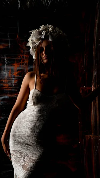美しいセクシー女性で白いドレスと花の花輪ポーズオンダークスタジオの背景 — ストック写真