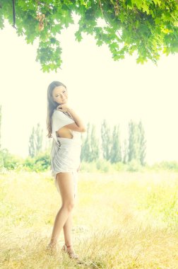 Güzel genç kız yaz parkında ağaçların arasında poz veriyor.