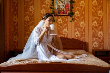 Beyaz elbiseli gelin düğünden önce odada poz veriyor.