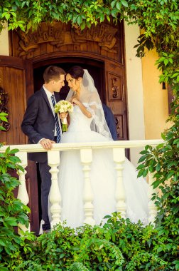 Gelin ve damat yeşil yapraklarla birlikte balkonda poz veriyorlar.