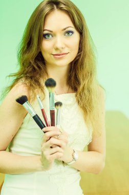 Yüzünde makyaj fırçası olan güzel genç bir kadın.