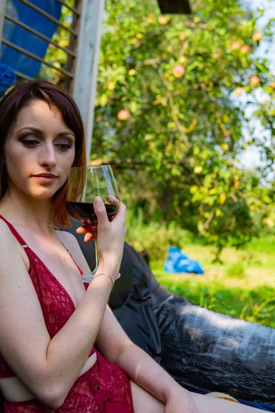 Jeune femme se détendre et boire un verre de vin rouge sur le balcon au coucher du soleil le soir . — Photo