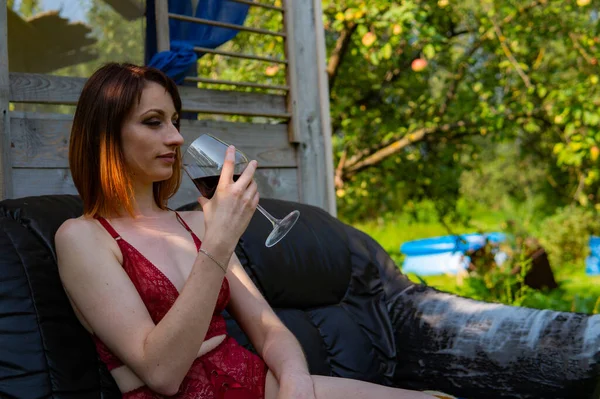 Jeune femme se détendre et boire un verre de vin rouge sur le balcon au coucher du soleil le soir . — Photo