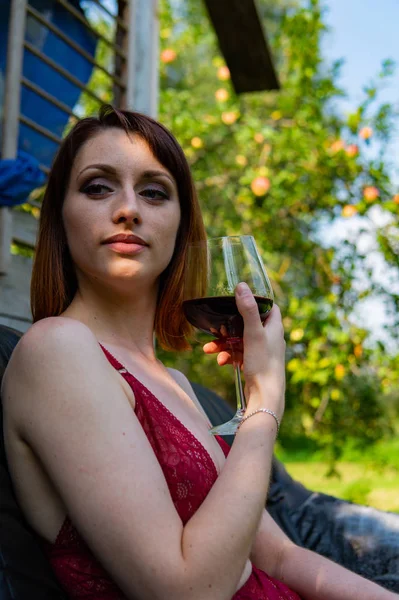 Mujer joven es relajarse y beber una copa de vino tinto en el balcón al atardecer por la noche . —  Fotos de Stock