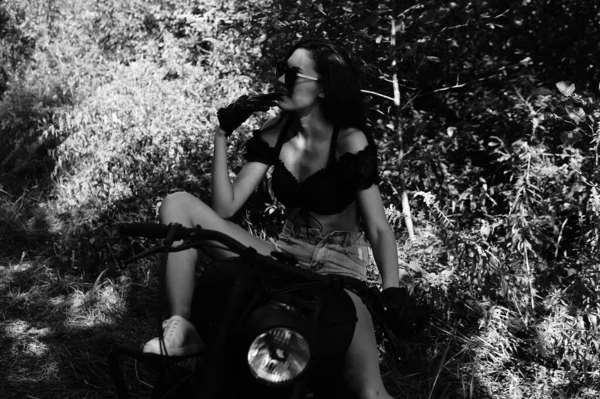 Молода сексуальна жінка з довгим хвилястим волоссям у шкіряному одязі та сонцезахисних окулярах позує біля мотоцикла. Чорно-біле фото . — стокове фото