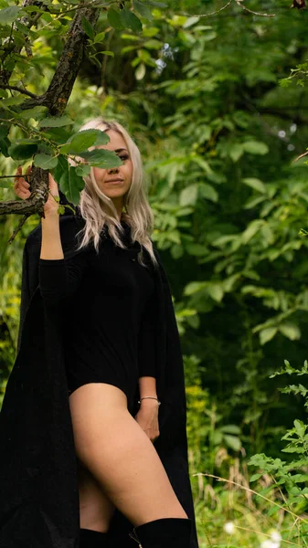 Sexy blonde woman in black cloak nature — Stock fotografie